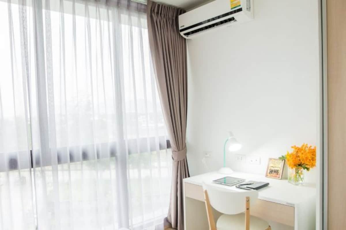A modern room with a desk, chair, air conditioning unit, and a window with sheer curtains.
