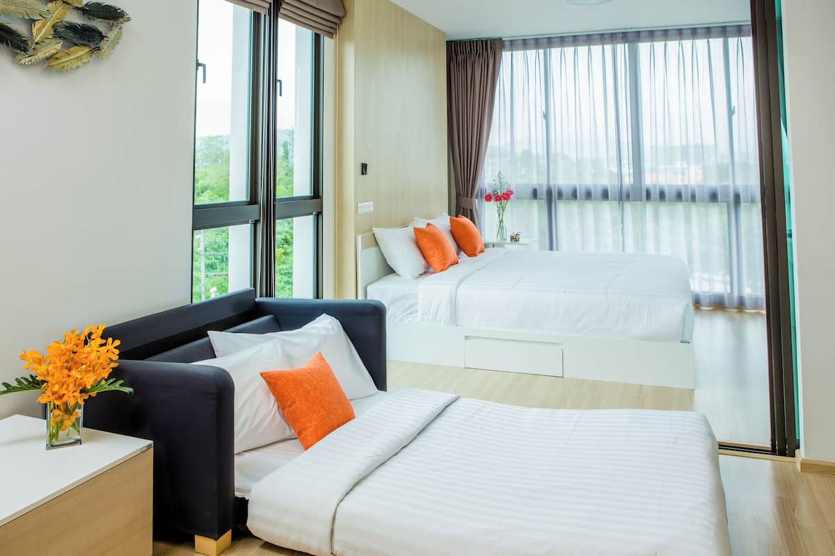 Quarto de hotel com uma cama grande, uma cama menor, um sofá e uma mesinha de cabeceira com um vaso de flores.
