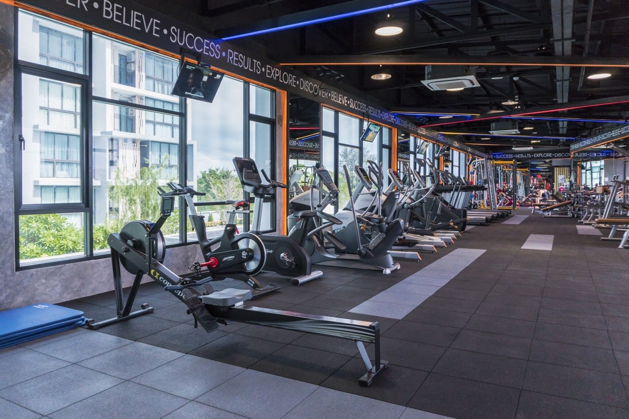 Un gimnasio con máquinas de cardio, bancos de pesas y un ventanal con vistas a la ciudad.