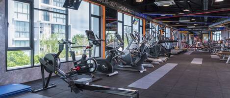 Un gimnasio con máquinas de cardio, bancos de pesas y un ventanal con vistas a la ciudad.
