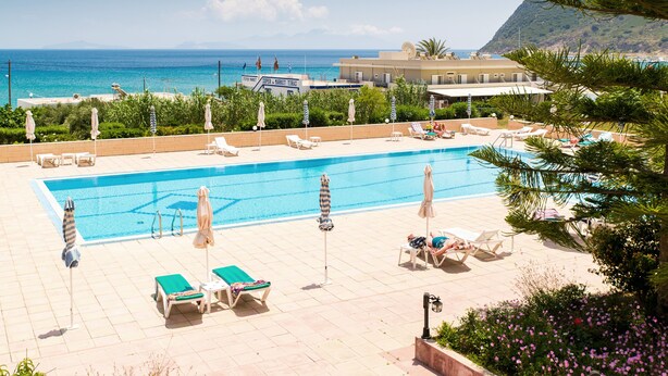 A pool area with lounge chairs and umbrellas, overlooking a beach and ocean. - Kontessa Apartments (Kos)