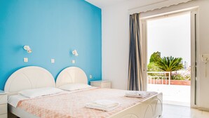 A bedroom with a bed, white headboard, bedside tables, and a view of the outdoors through a window. - Kontessa Apartments (Kos)