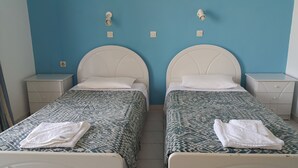 A twin room with two beds, each with a headboard, white bedding, and a patterned bedspread. There are two bedside tables with lamps and a wall socket above each bed. - Kontessa Apartments (Kos)