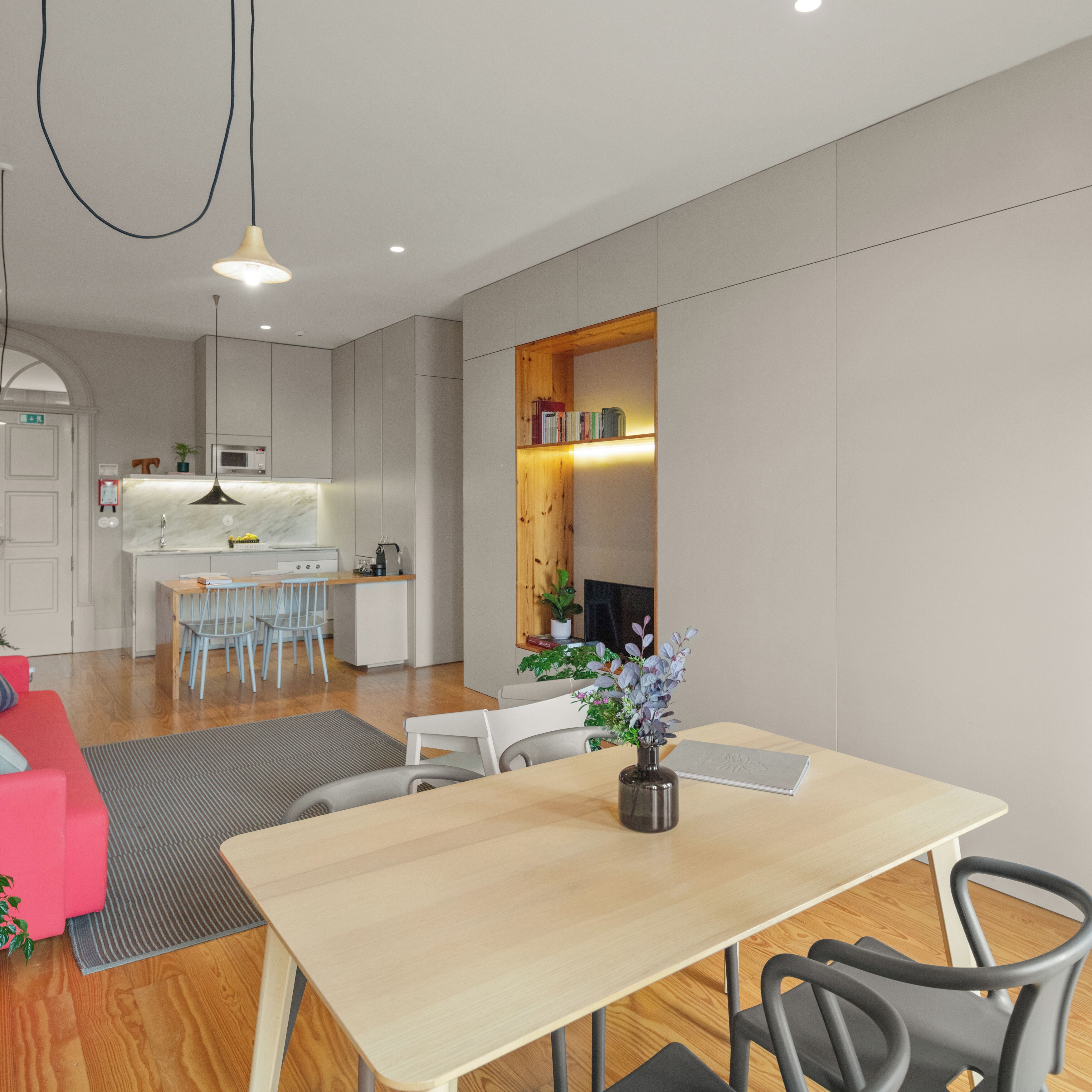 A modern kitchen with white cabinets, a dining area with a wooden table and chairs, and a living room with a red sofa.