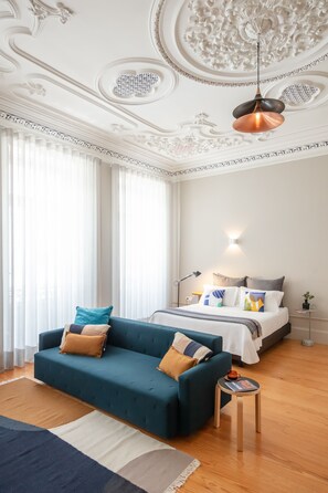 A modern hotel room with a blue sofa, a bed with white bedding, and a decorative ceiling. - Baumhaus Serviced Apartments (Porto)