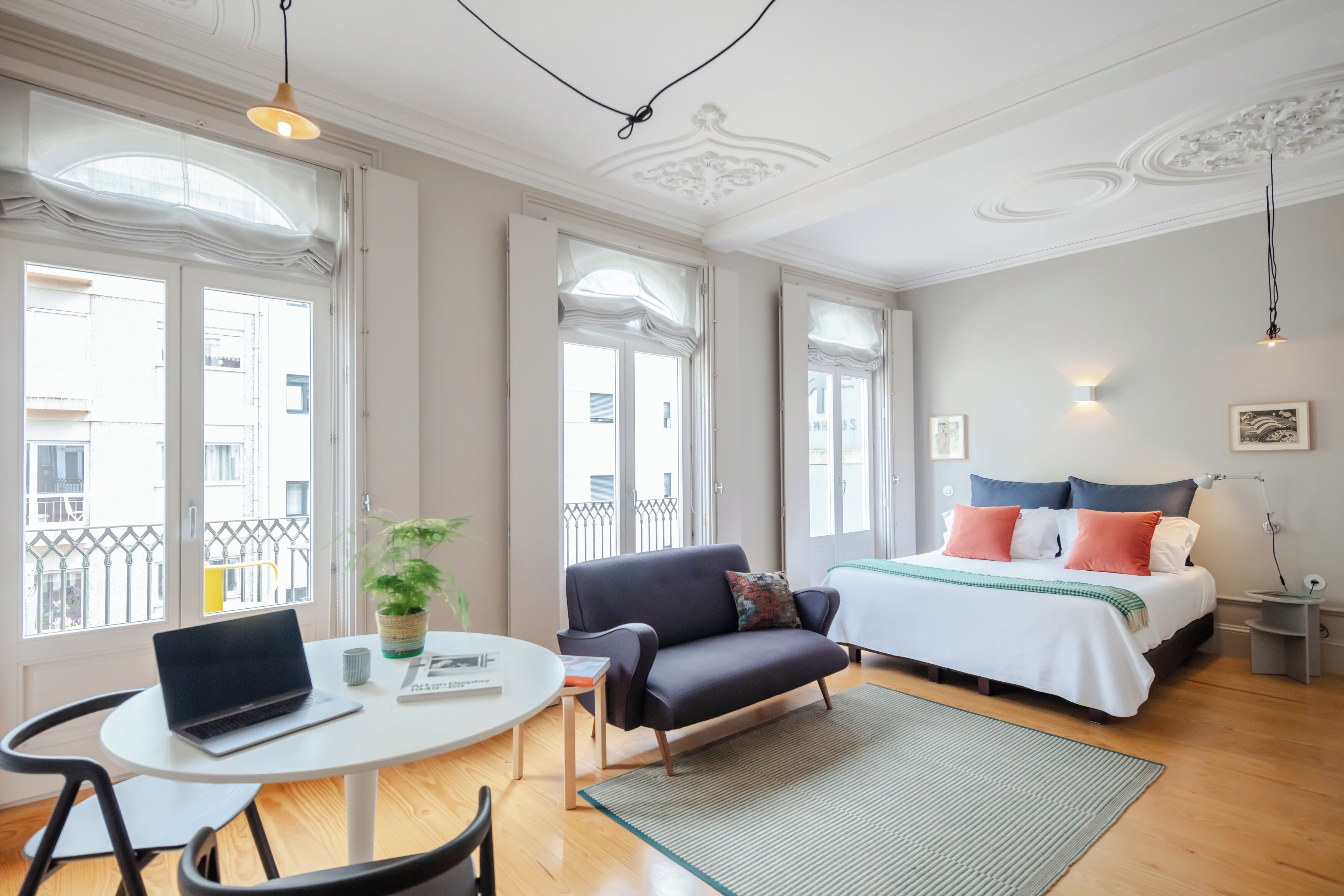 A modern bedroom with a bed, a sofa, a dining table, and a laptop.