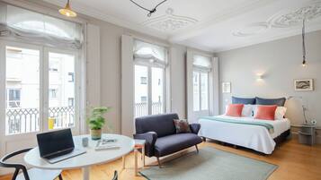 A modern bedroom with a bed, a sofa, a dining table, and a laptop.