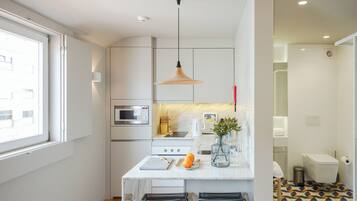 A modern kitchen with a white countertop, a hanging pendant light, and a dining area with two chairs.