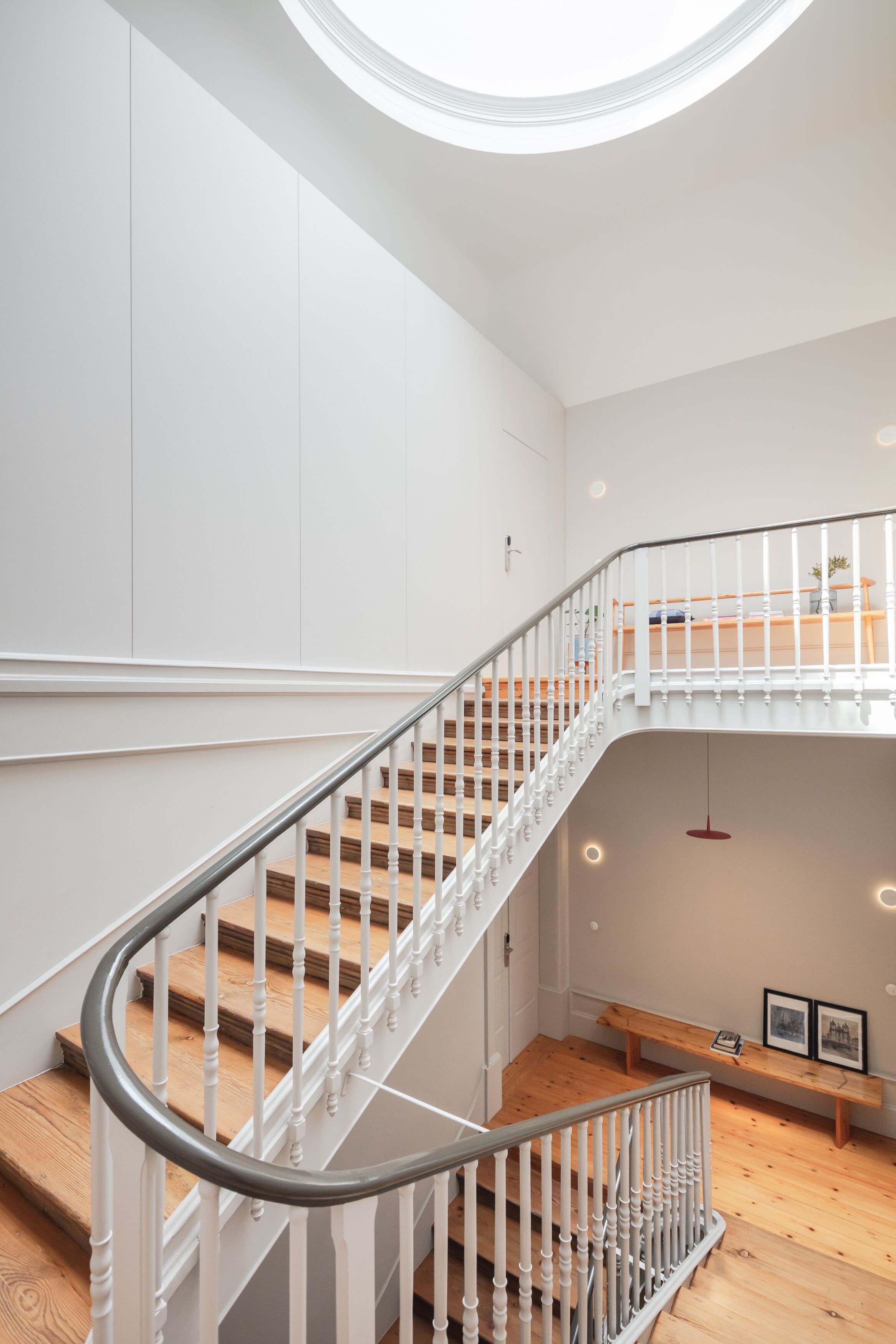 A modern staircase with white railings and wooden steps, leading to a second-floor landing with a bench and framed pictures.