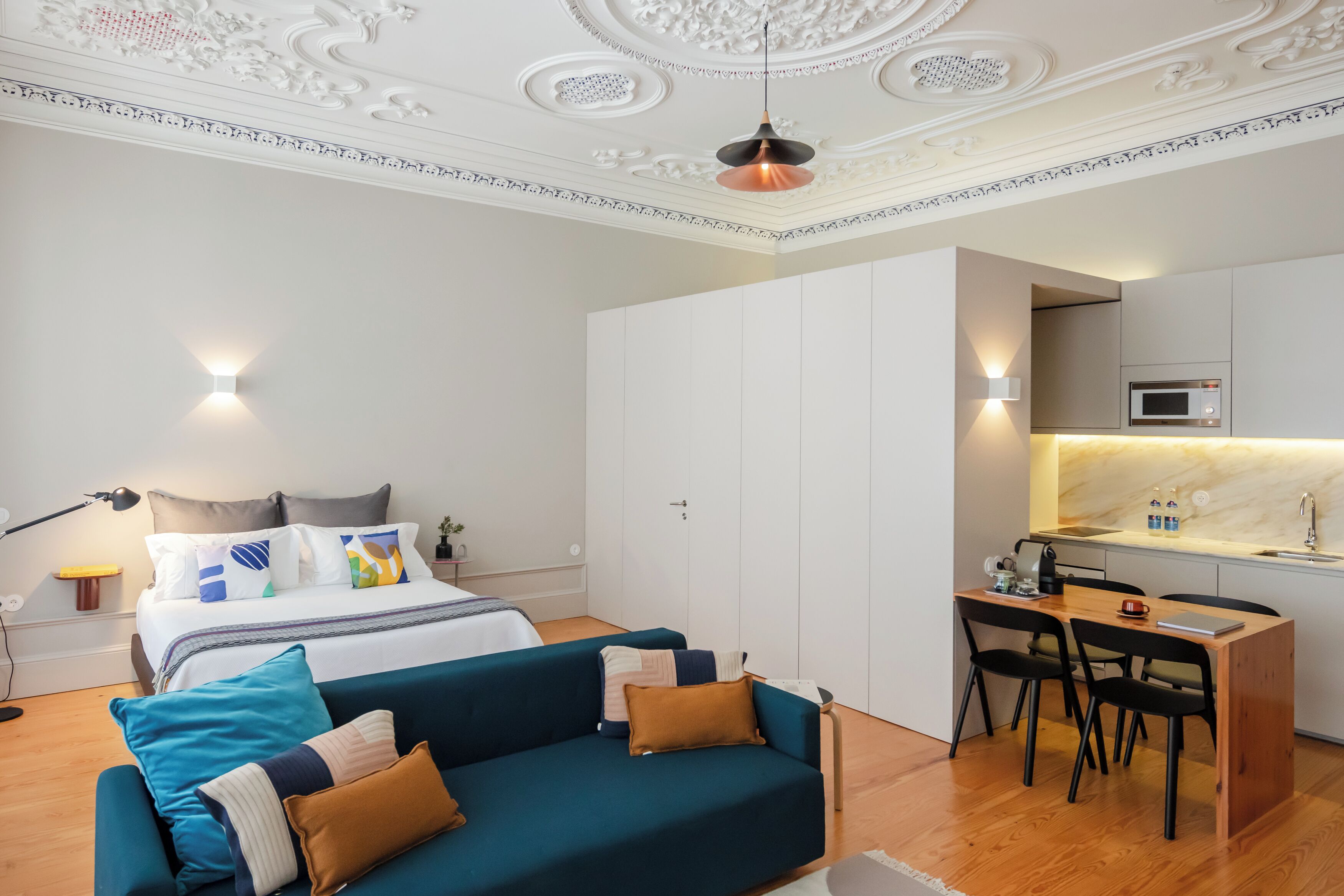 A modern bedroom with a bed, a blue sofa, a desk with a chair, and a kitchenette.