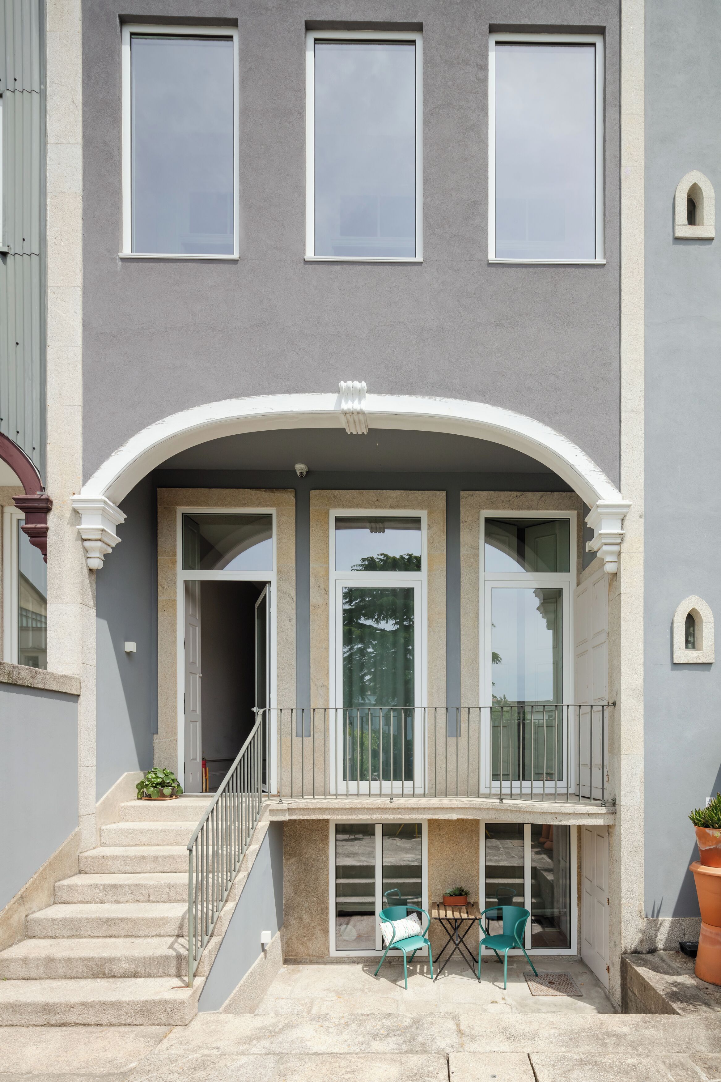A building with a covered balcony, a staircase, and two potted plants.