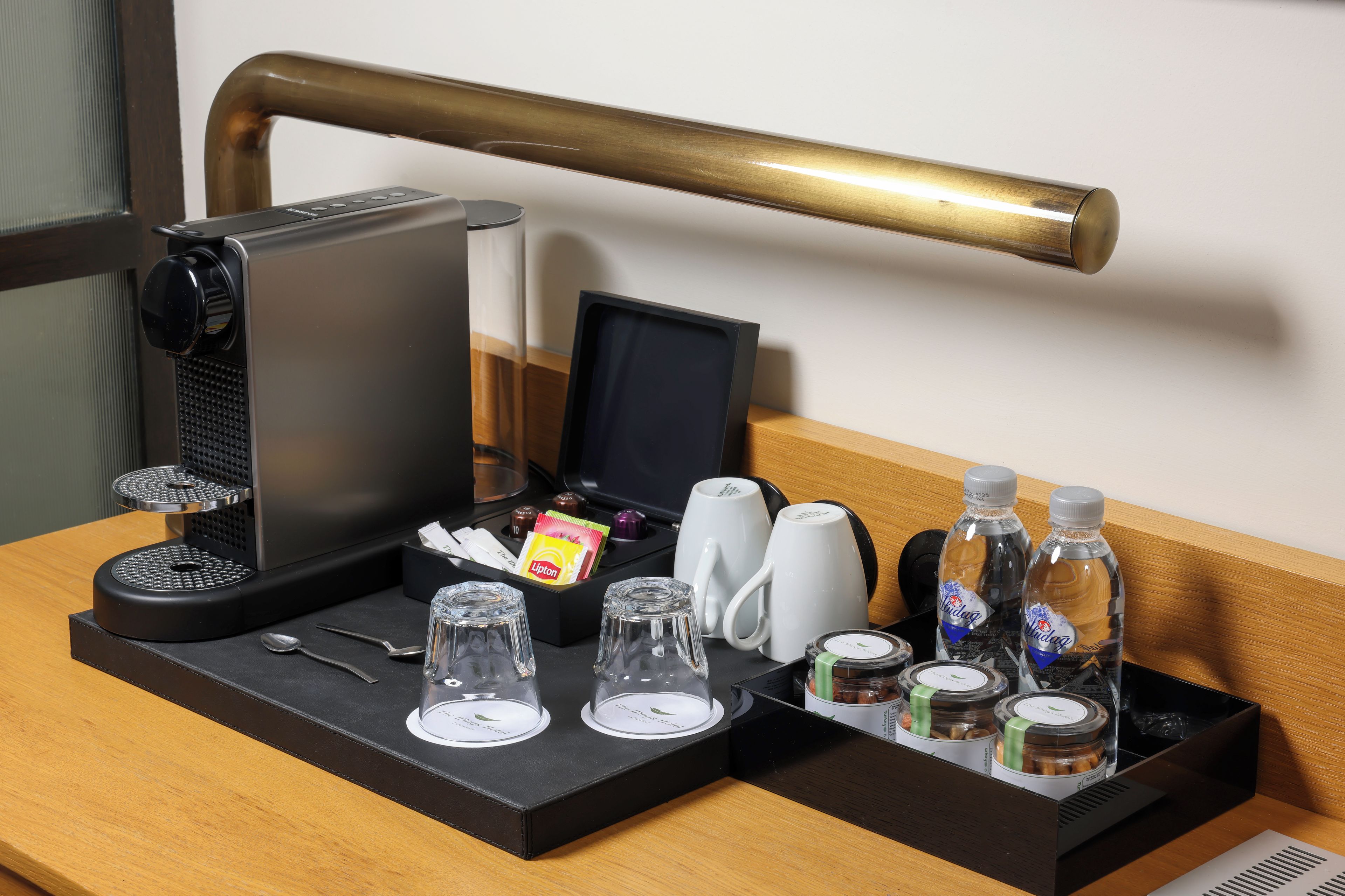 A hotel room with a coffee maker, tea set, glasses, and bottled water on the table.