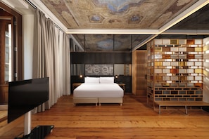 Ein modernes Hotelzimmer mit einem großen Bett, einem Flachbildfernseher, Holzboden und einer dekorativen Decke.