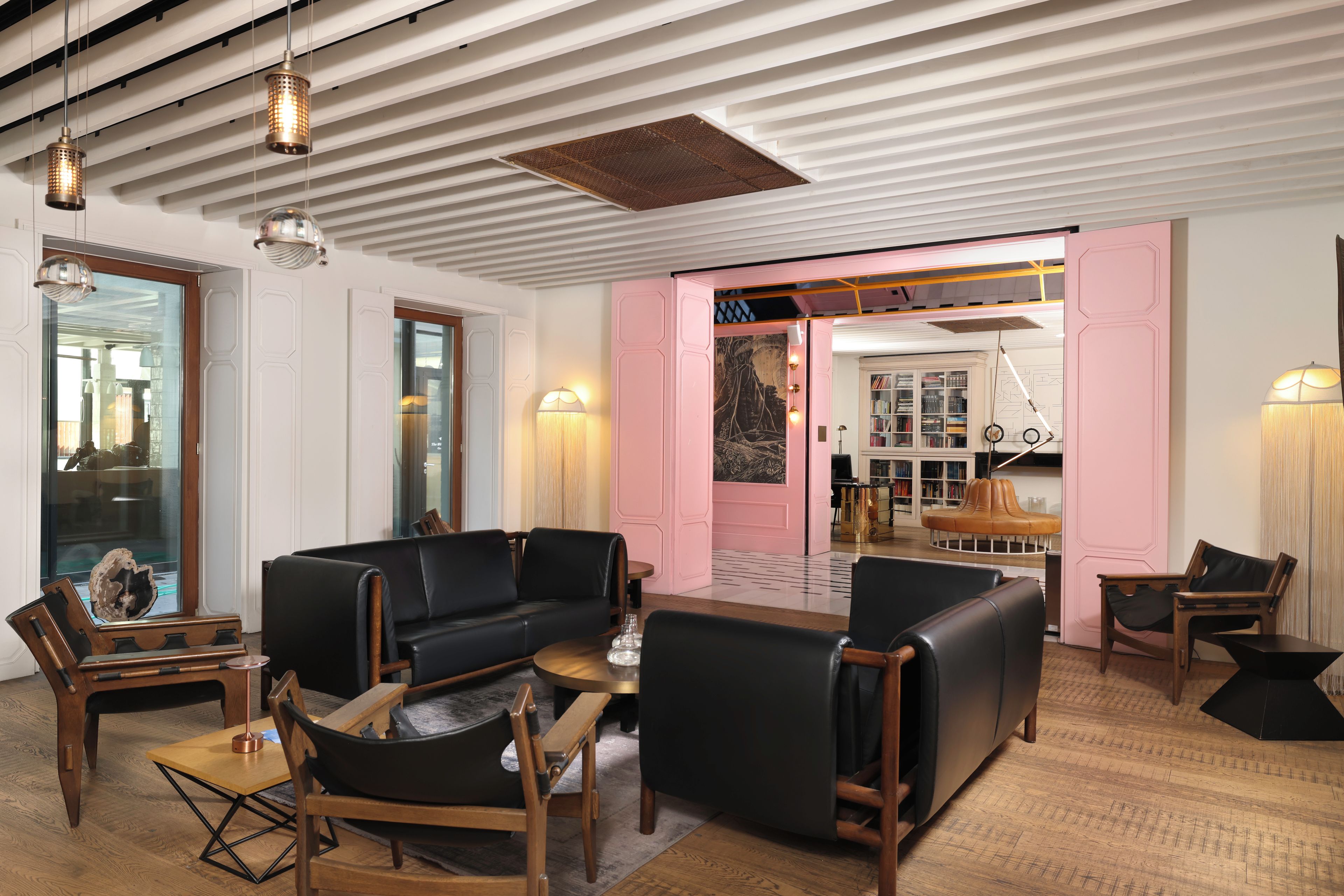 Un interior moderno con un sofá de cuero negro, sillas de madera, una mesa de centro y una pared de acento rosa.