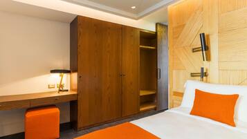 A hotel room with a bed, a wooden wardrobe, a desk with a lamp, and a wall-mounted TV.
