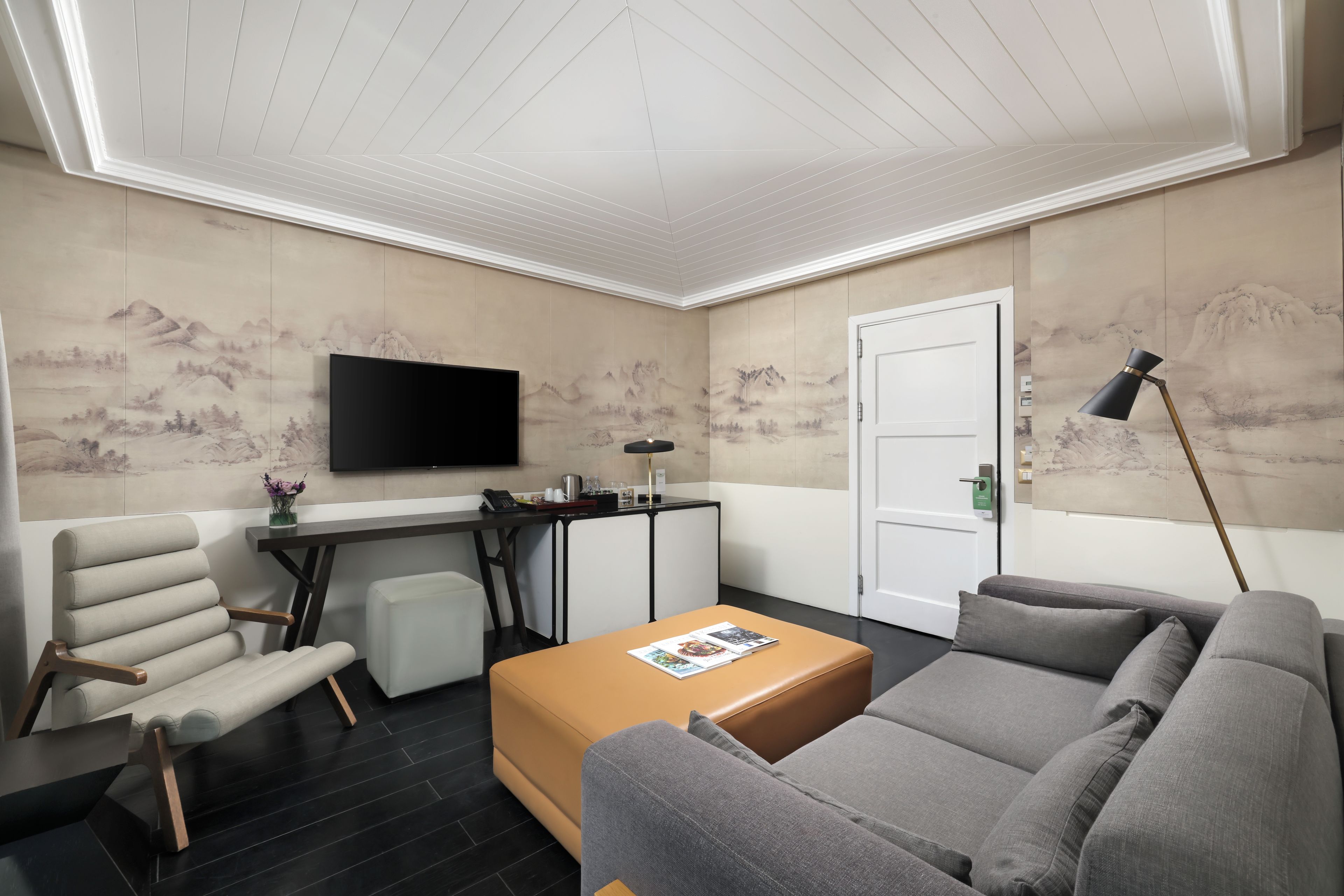 A modern living room with a flat-screen TV, a sofa, a coffee table, and a desk with a lamp.