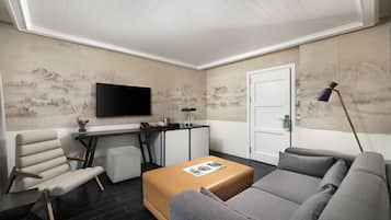A modern living room with a flat-screen TV, a sofa, a coffee table, and a desk with a lamp.