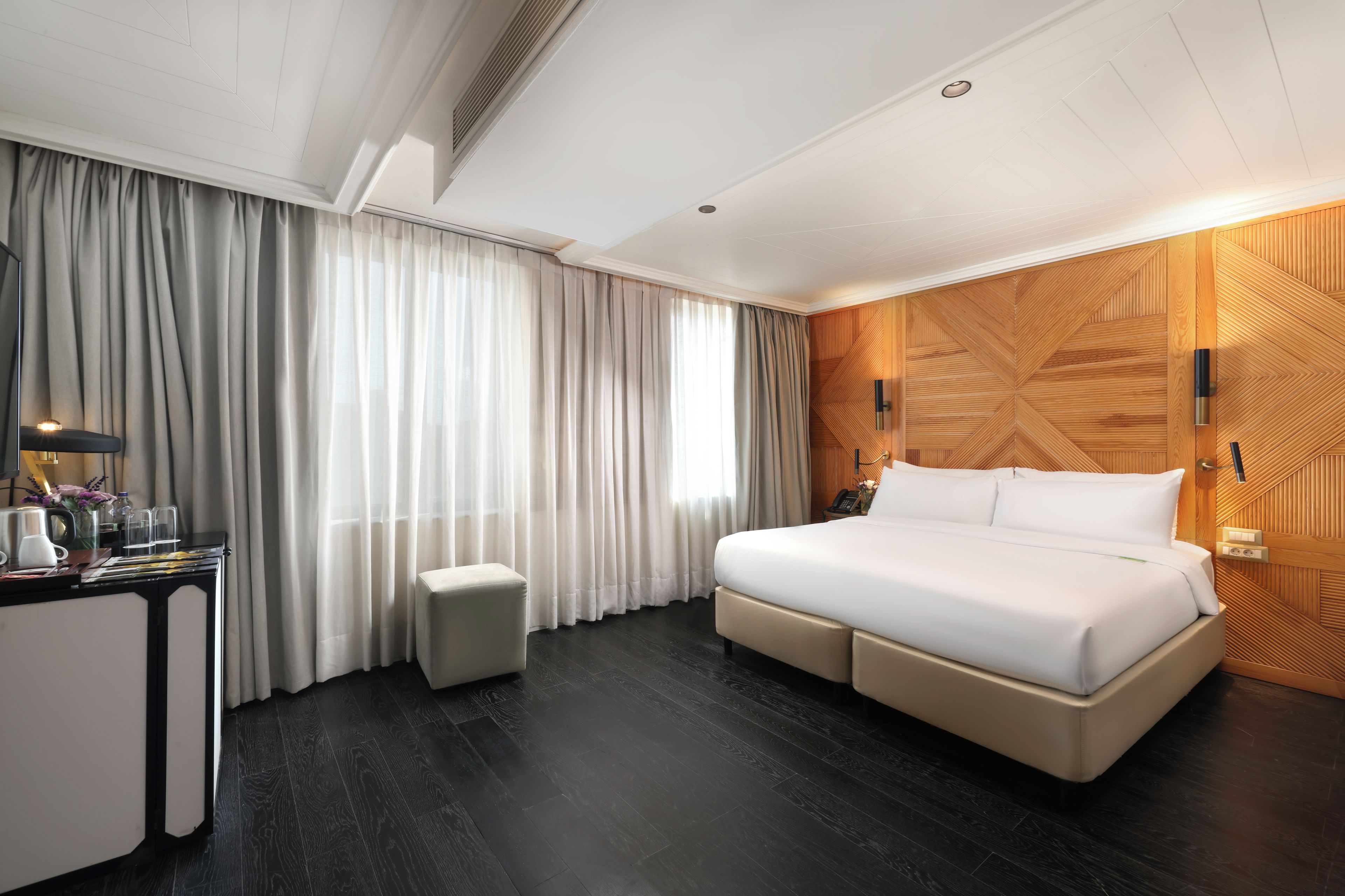Una camera d'albergo con un letto grande, una scrivania con lampada, uno sgabello piccolo e un pannello decorativo in legno.