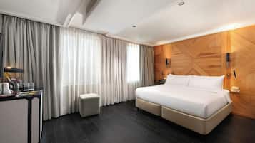 Una camera d'albergo con un letto grande, una scrivania con lampada, uno sgabello piccolo e un pannello decorativo in legno.
