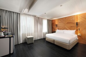 A hotel room with a large bed, a desk with a lamp, a small stool, and a wooden accent wall. - The Wings Hotels Collection (Istanbul)