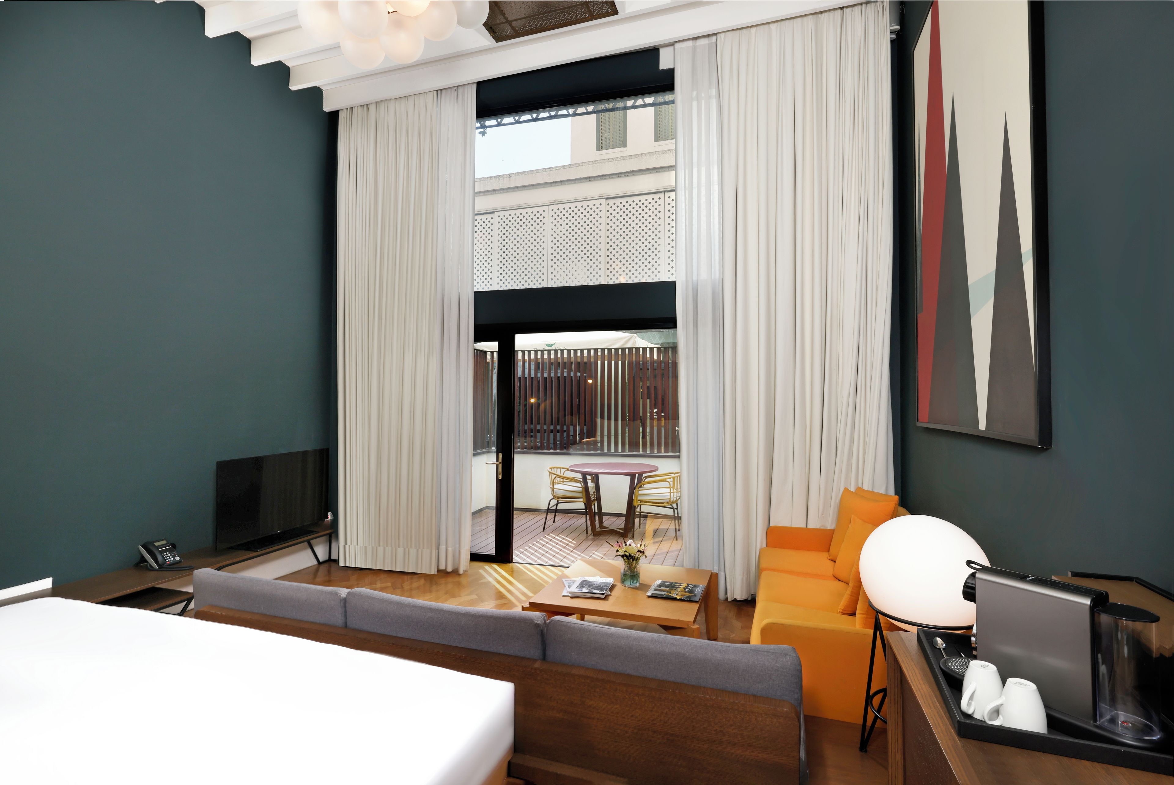 Una habitación de hotel moderna con sofá, una mesa de centro, televisión y escritorio con cafetera.