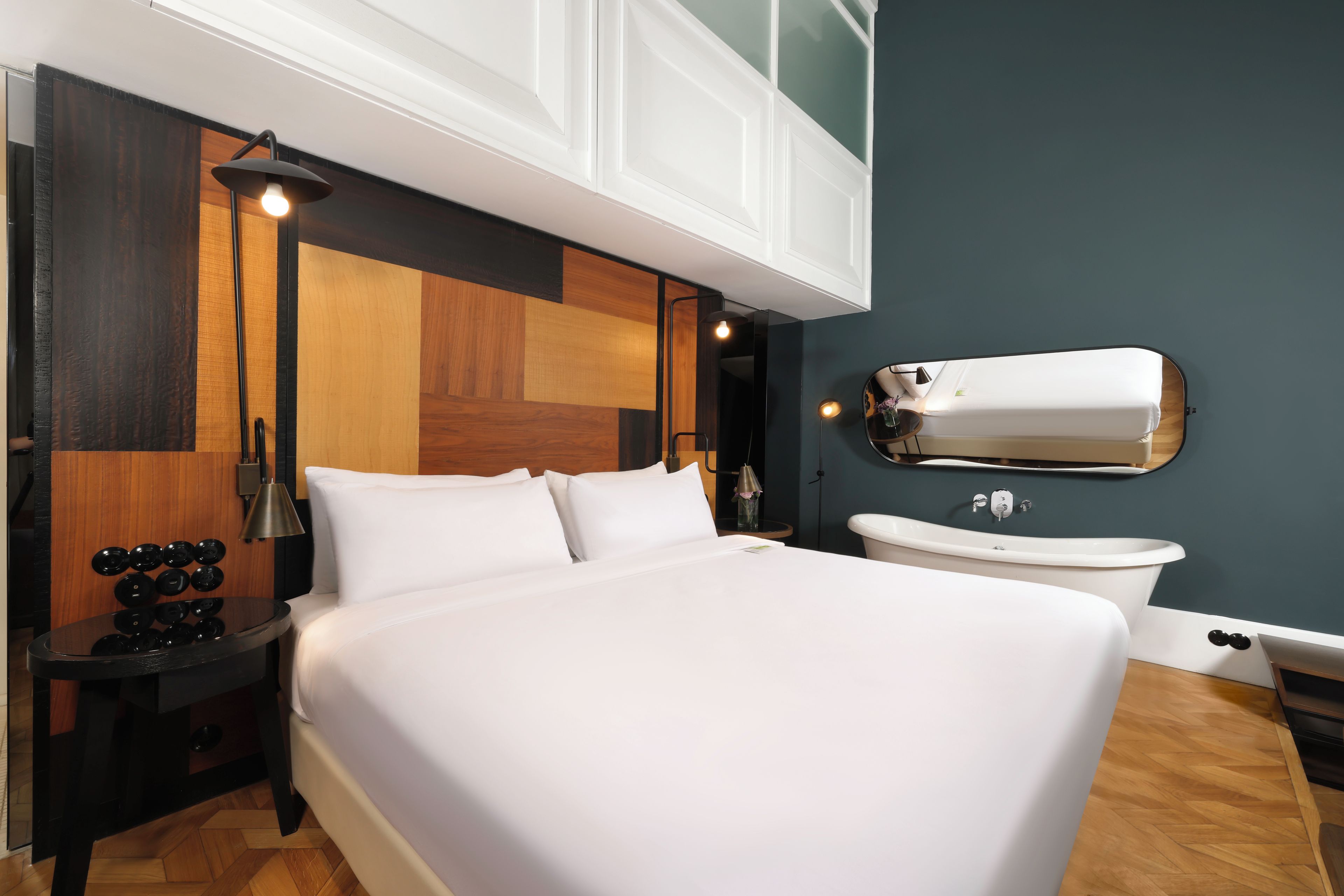 Habitación de hotel moderna con una cama grande, lámparas de noche, un espejo redondo y una bañera blanca.