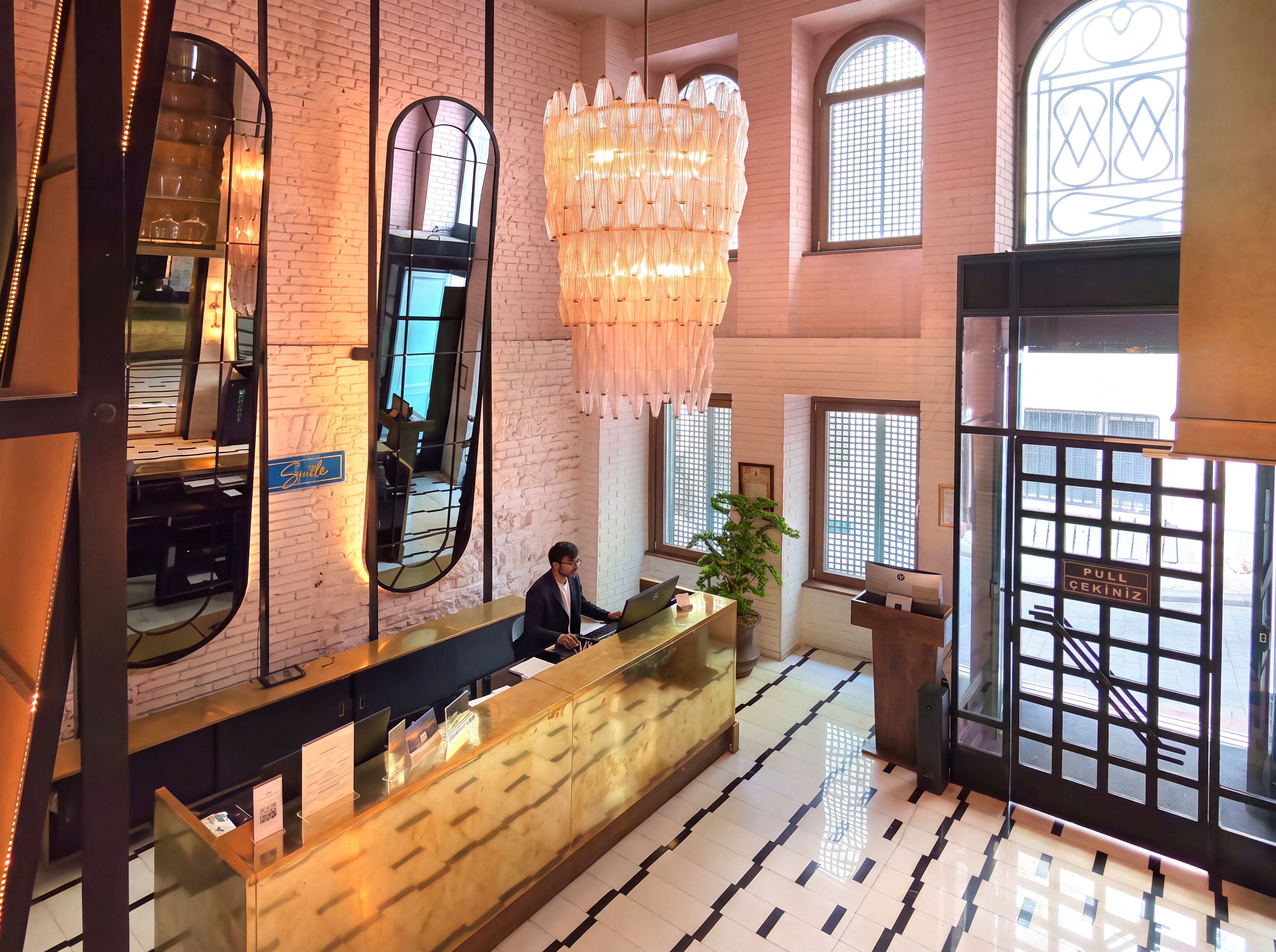 Ein Hotel-Empfangsbereich mit modernem Design, der eine Rezeption, eine große Chandelier und einen Blick auf die Straße durch eine Glastür bietet.