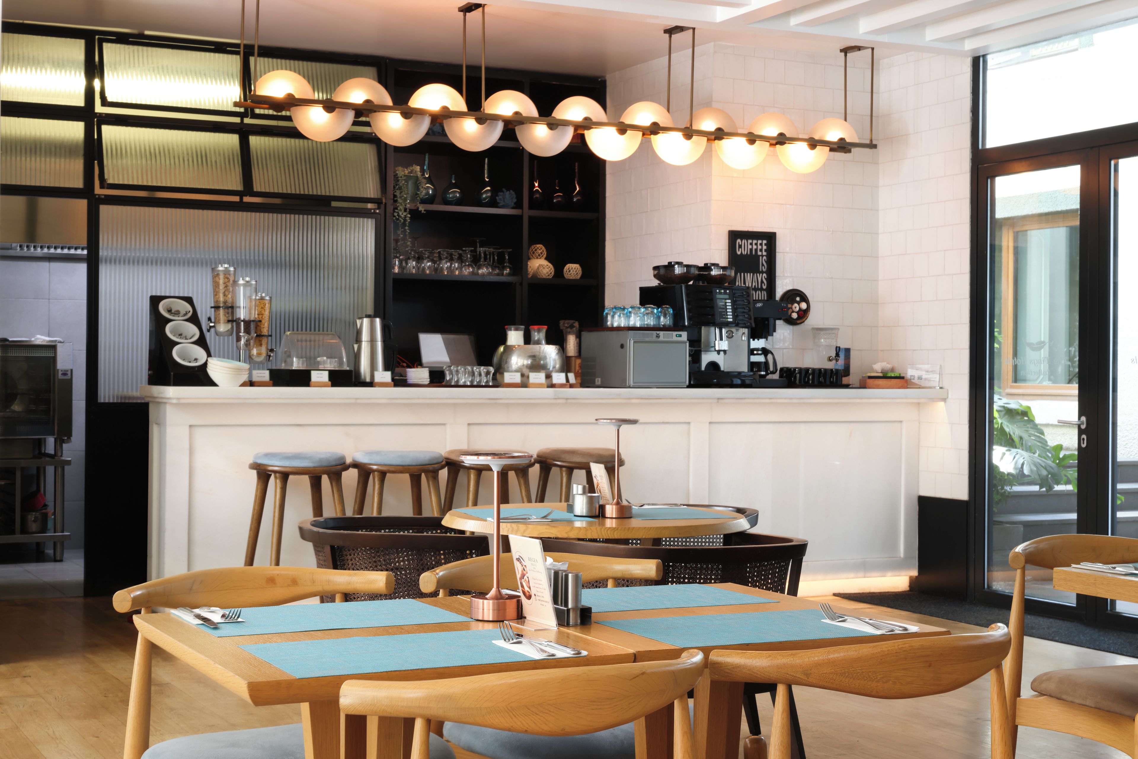 Interior de una cafetería moderna con mesas y sillas de madera, una zona de bar y una variedad de vasos a la vista.