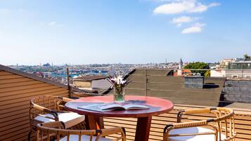 A rooftop terrace with a round table, two wicker chairs, and a view of a cityscape.