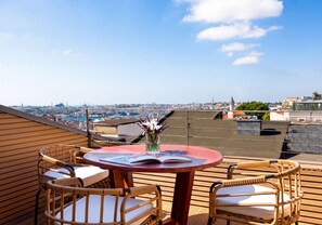 A rooftop terrace with a round table, two wicker chairs, and a view of a cityscape.