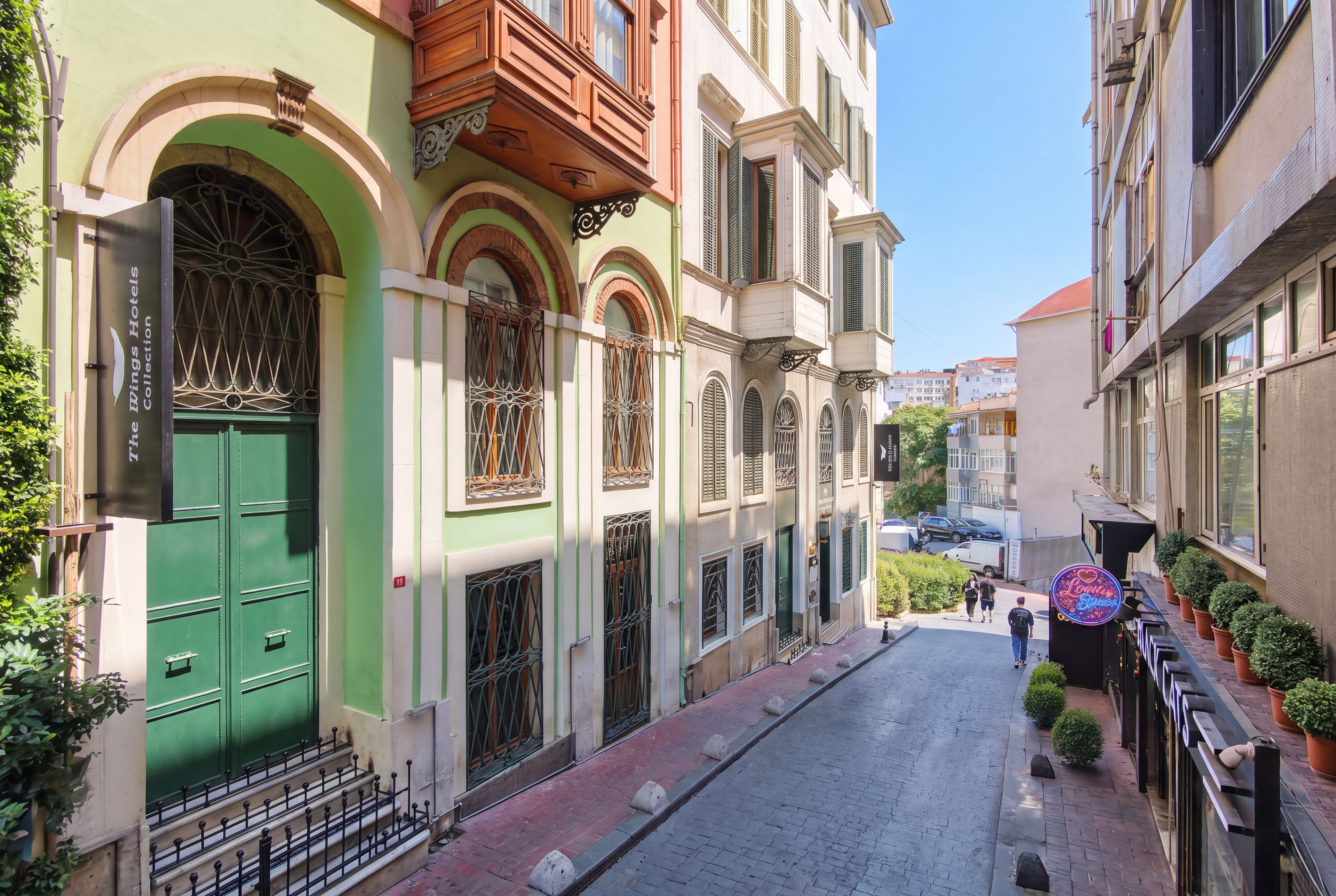 Una calle estrecha con edificios que tienen ventanas y puertas arqueadas, un letrero de hotel visible y un cielo despejado.