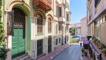 Una calle estrecha con edificios que tienen ventanas y puertas arqueadas, un letrero de hotel visible y un cielo despejado.