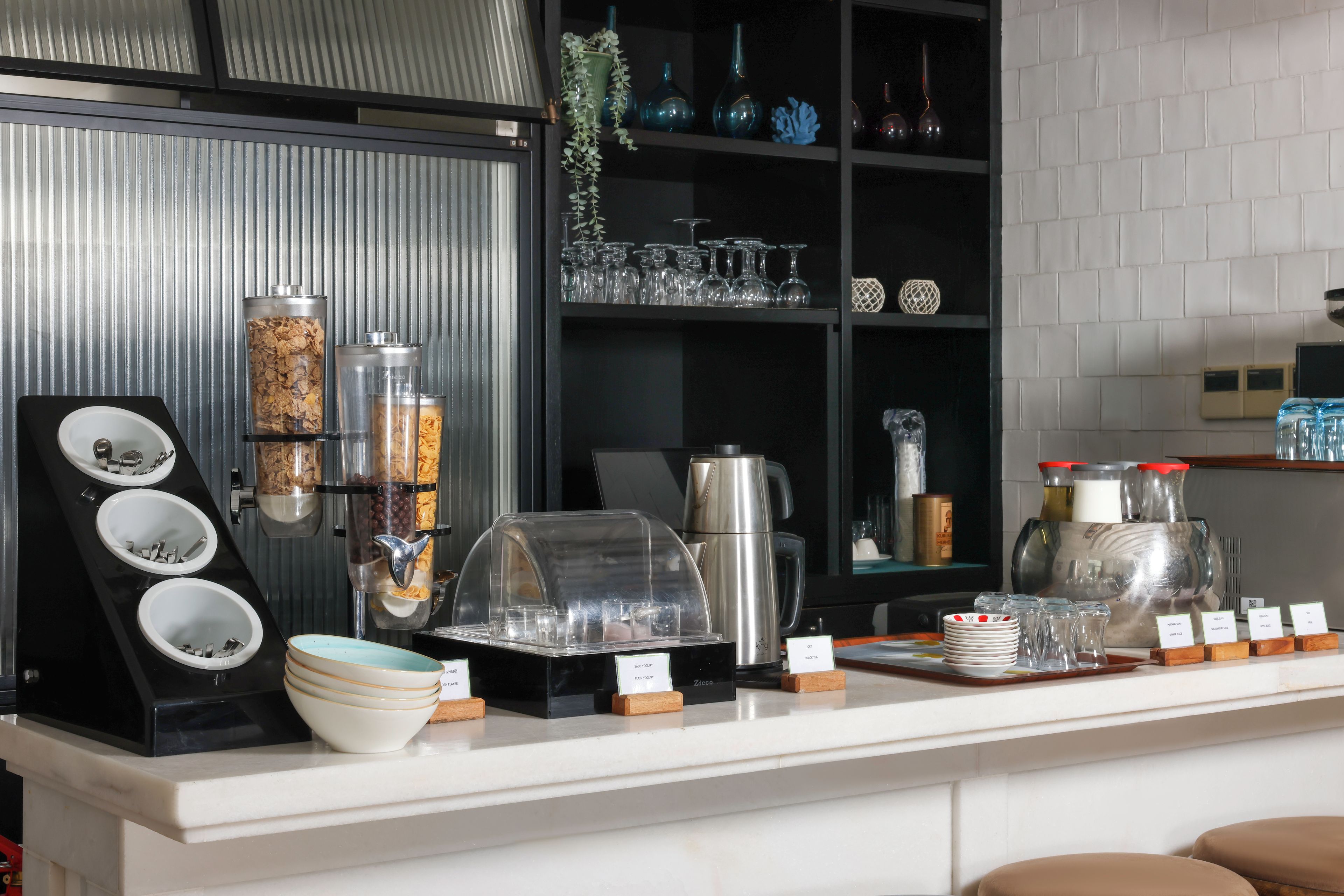 Una barra de desayuno con dispensador de cereales, cafetera y diferentes recipientes de vidrio.
