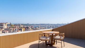Eine Dachterrasse mit Holzboden, einem runden Tisch und vier Korbstühlen.