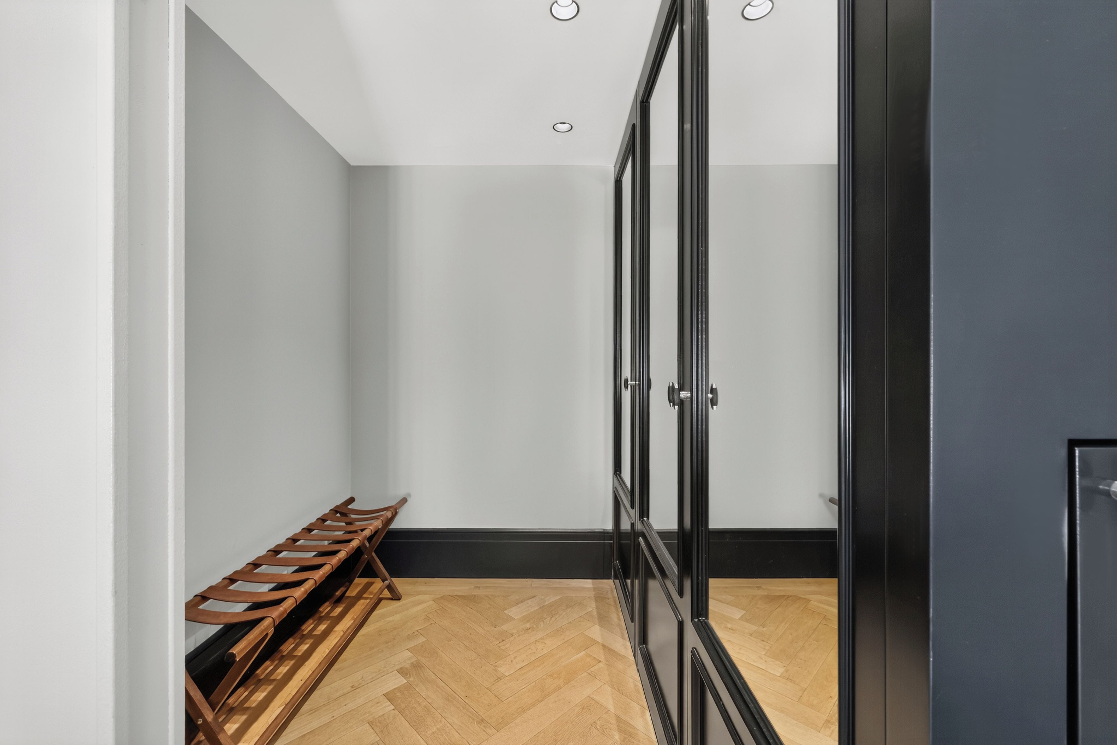 Una habitación con un banco de madera, una puerta negra y un piso con estampado tipo espiga.