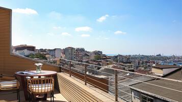 Una terraza en la azotea con mesa y sillas, con vistas a un paisaje urbano de edificios y al mar.