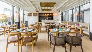 Een modern restaurant met houten tafels en stoelen, grote ramen en een plafond met een uniek ontwerp.