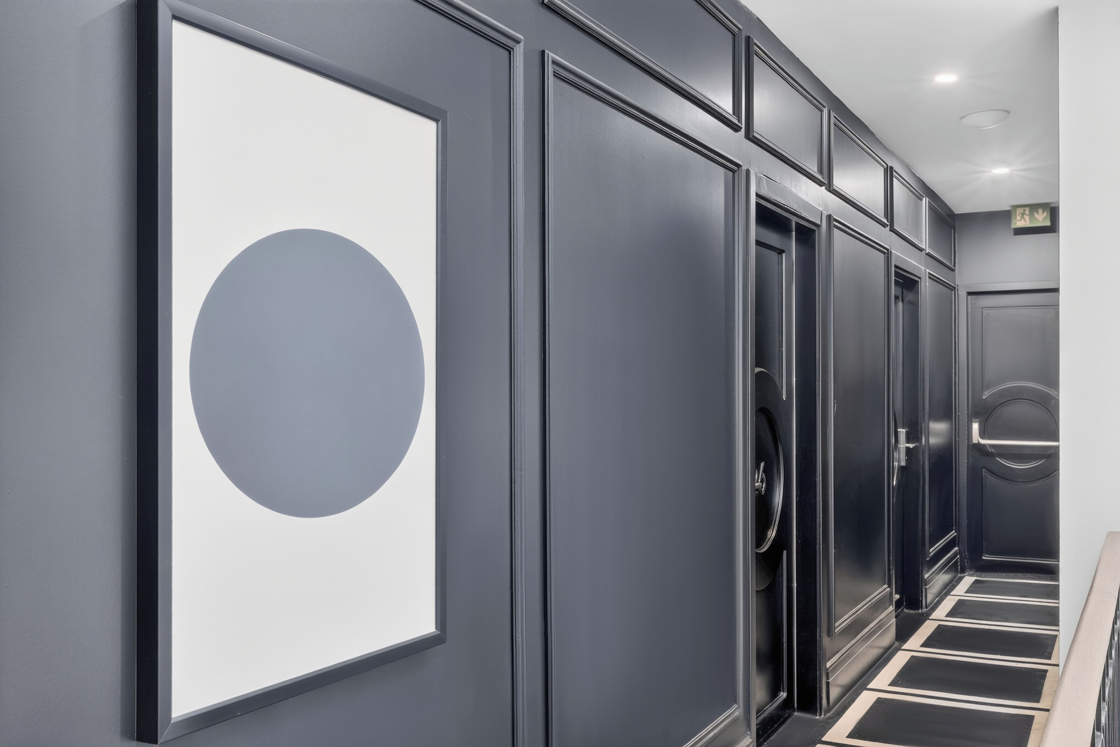 A hallway with a large framed artwork, a door with a circular handle, and a patterned floor.