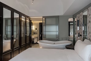 A modern bedroom with a large bed, a freestanding bathtub, and a walk-in closet with mirrored doors.