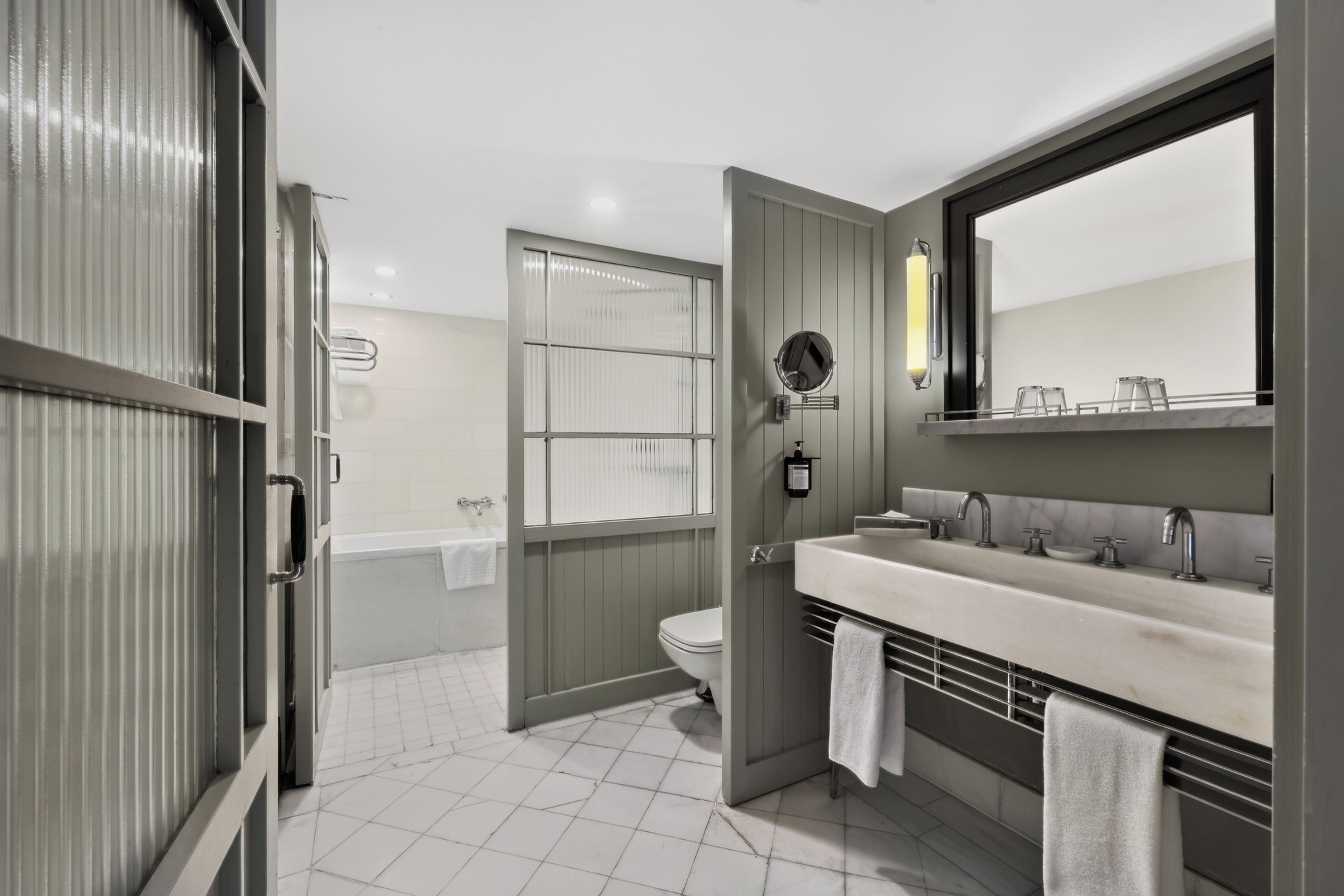 A modern bathroom with a large mirror, two sinks, and a toilet.