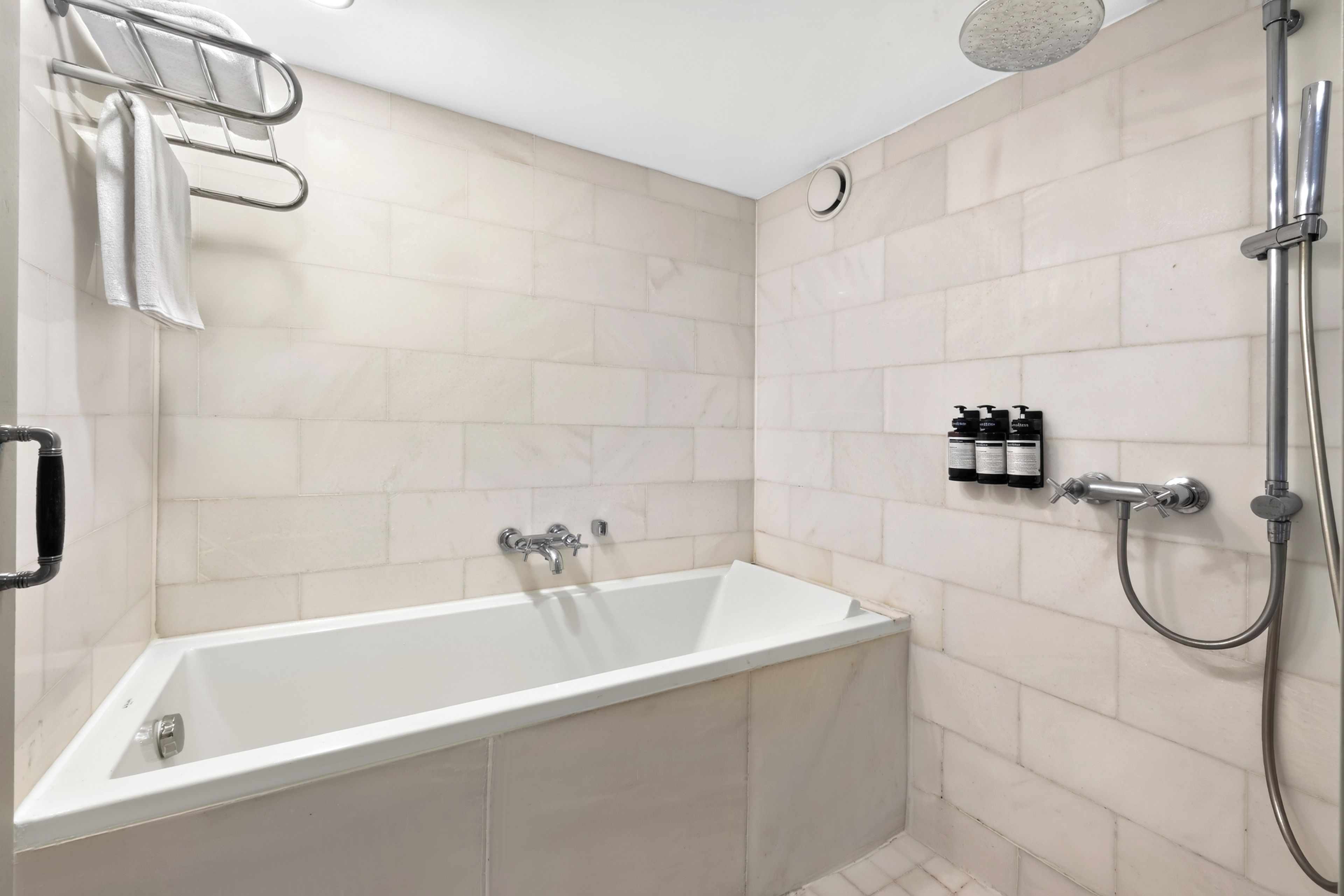 A modern bathroom with a bathtub, shower, and hand soap dispensers.