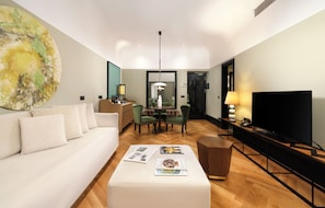Une chambre d’hôtel moderne avec un canapé blanc, un coin repas avec des chaises vertes, un téléviseur à écran plat et un grand tableau abstrait accroché au mur.