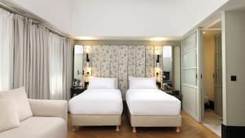 A hotel room with two single beds, a sofa, a nightstand with a lamp, and a mirror.
