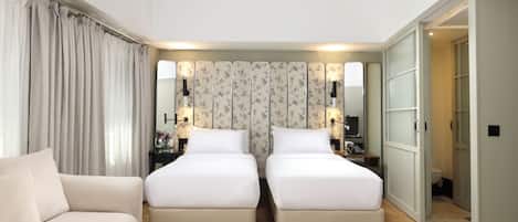 A hotel room with two single beds, a sofa, a nightstand with a lamp, and a mirror.