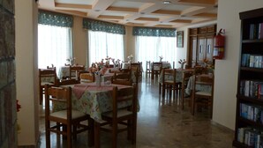 Comedor con mesas y sillas de madera, cubiertas con manteles florales. Se observan estanterías a la derecha.