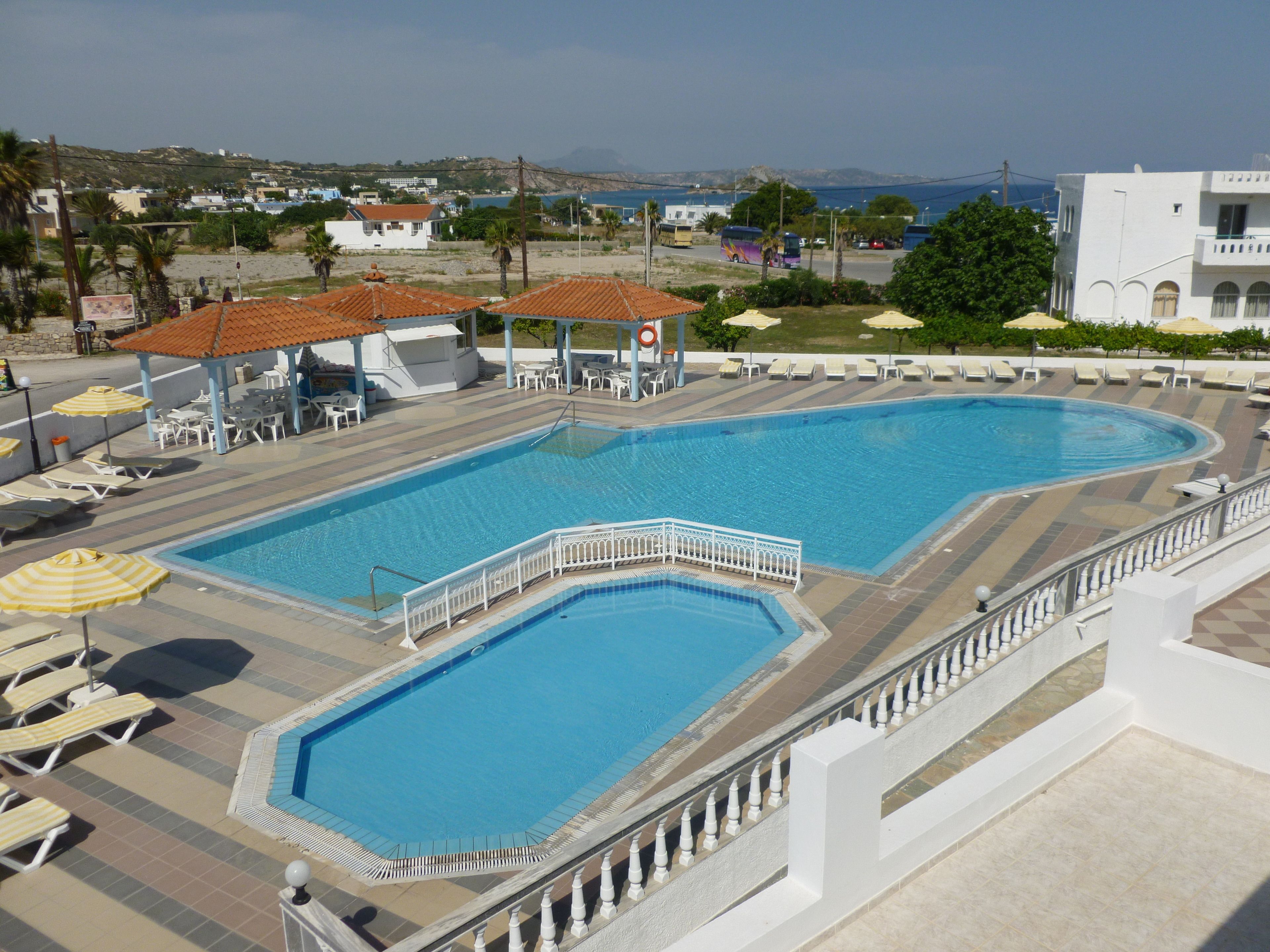 Una gran piscina rectangular con una barandilla decorativa blanca, rodeada de tumbonas y sombrillas.