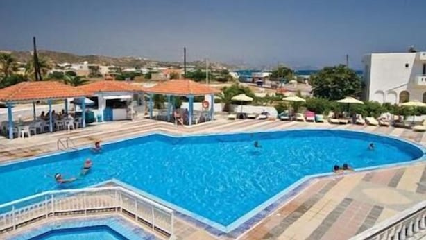 Una amplia piscina al aire libre con solárium de baldosas, rodeada de sillones y sombrillas, y vista al mar de fondo.