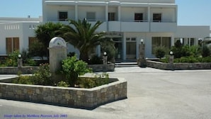 Un edificio moderno de dos pisos con fachada simétrica, una entrada central y un patio ajardinado con macetas de piedra y una palmera.