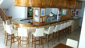 Zona de bar con armarios de madera, una barra curva y taburetes blancos.