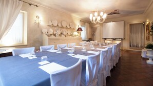A conference room with a long table, white chairs, a projector screen, and a chandelier.